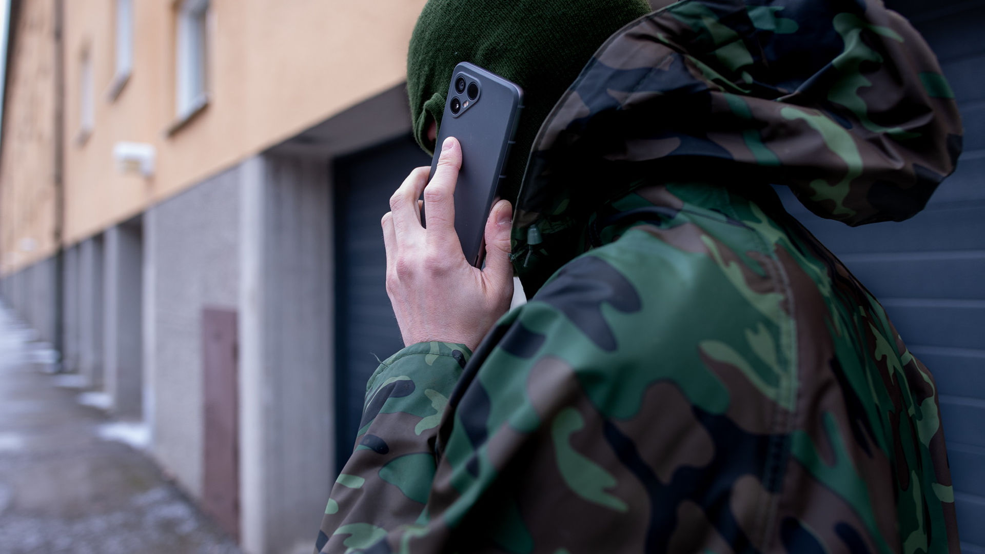En man går utmed en fasad med ryggen vänd mot kameran, han pratar i mobiltelefon, man ser inte hans ansikte.