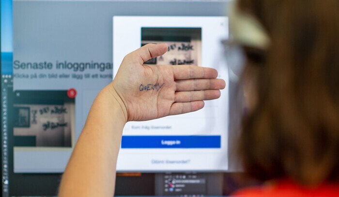 En person sitter framför datorn och håller upp sin hand där lösenordet qwerty syns.