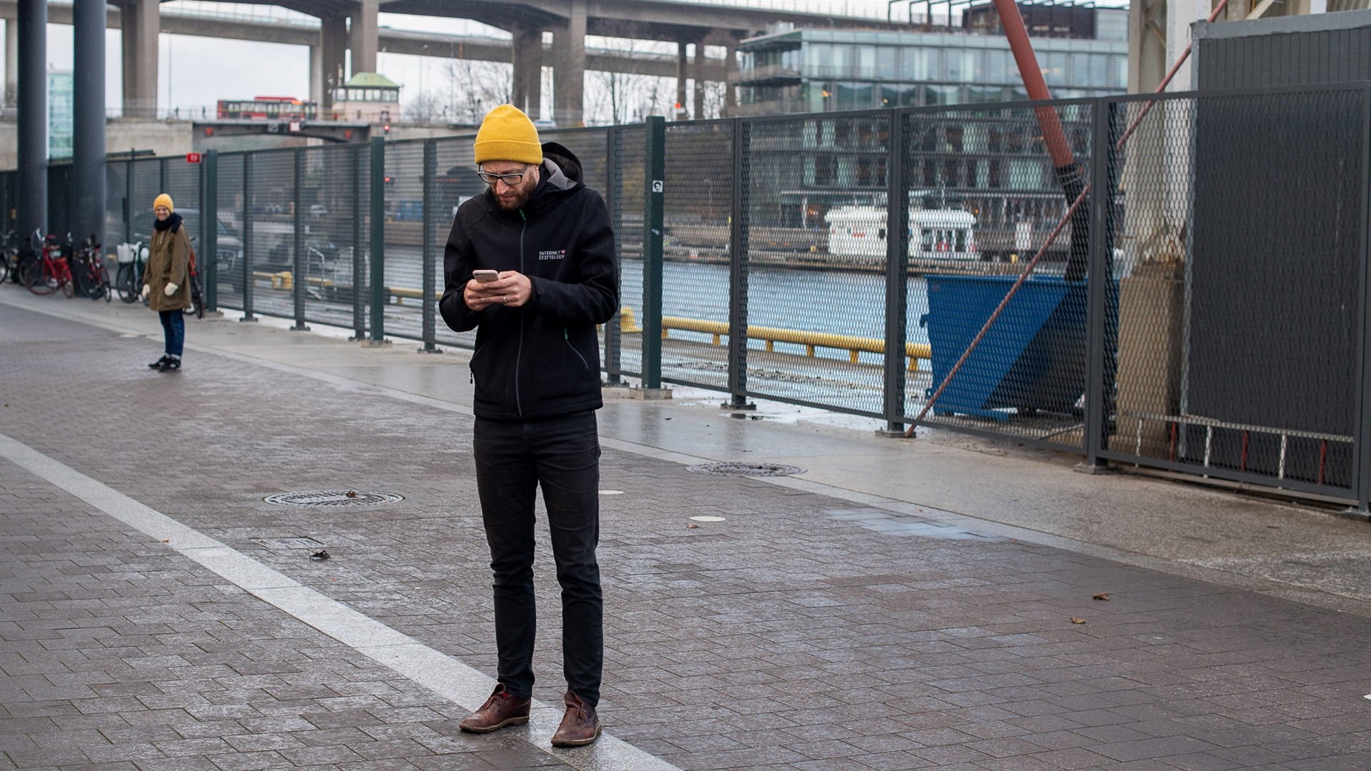 En man står utomhus med mobilen i händerna.