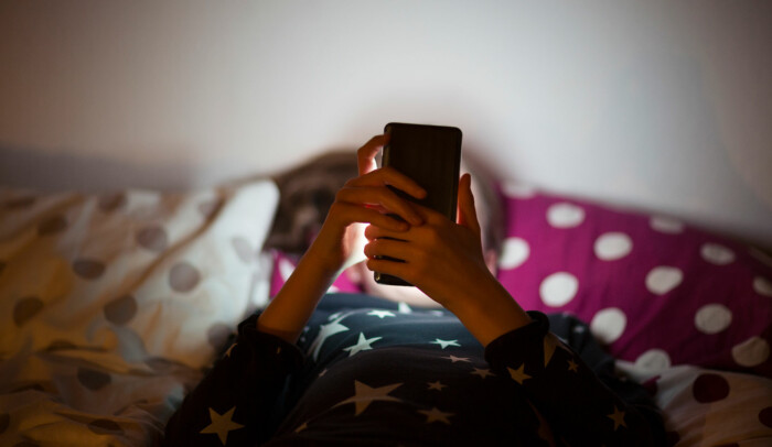 Barn som ligger i sängen och tittar på mobilen