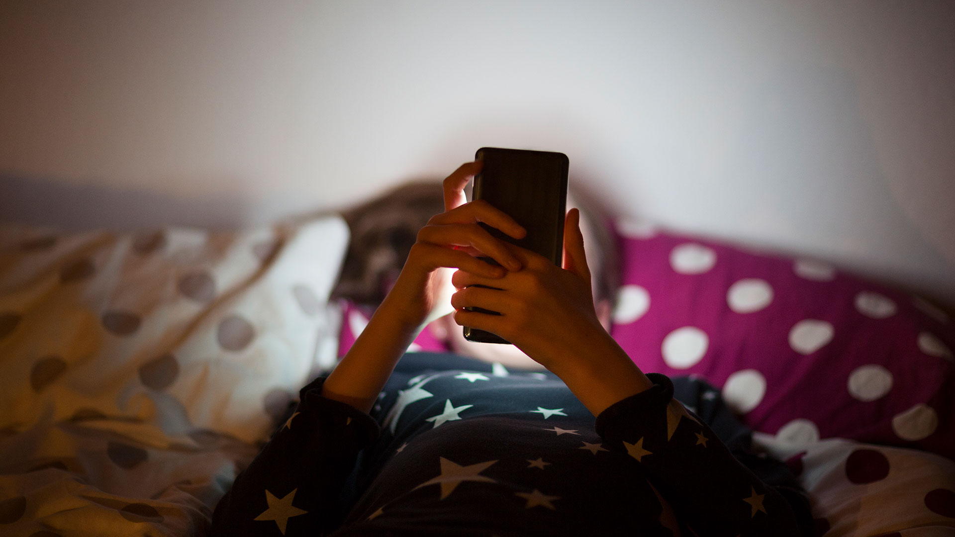 Barn som ligger i sängen och tittar på mobilen