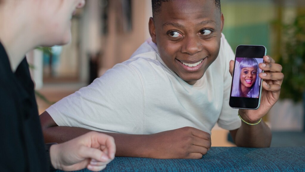 En ung kille visar upp en deepfake-bild på sig själv med annan frisyr på mobilen.