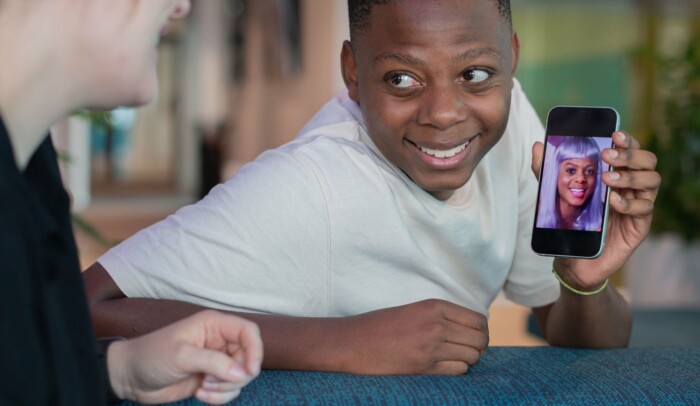 En ung kille visar upp en deepfake-bild på sig själv med annan frisyr på mobilen.