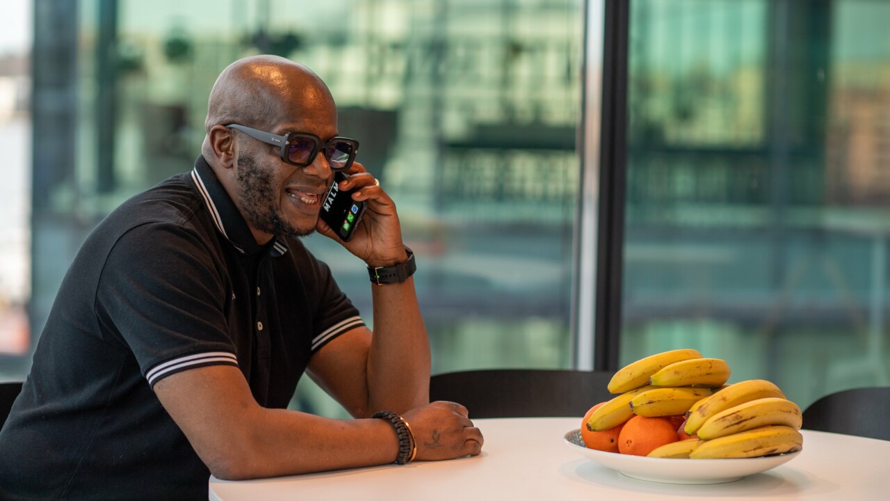 En man sitter vid ett bord och pratar i sin smartphone