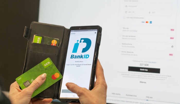 Någon håller i en mobil med bank-id på skärmen och ett kreditkort i andra handen.