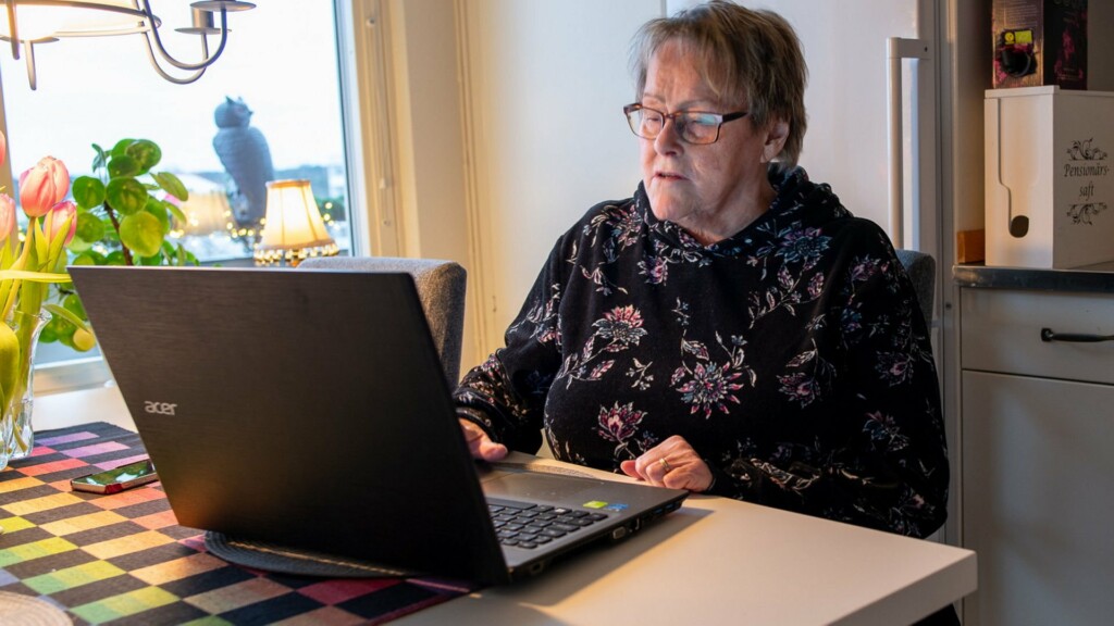 En kvinna sitter vid ett köksbord med laptop framför sig