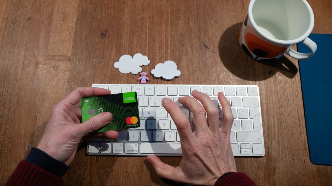Händer som håller i ett betalkort och trycker på ett tangentbord