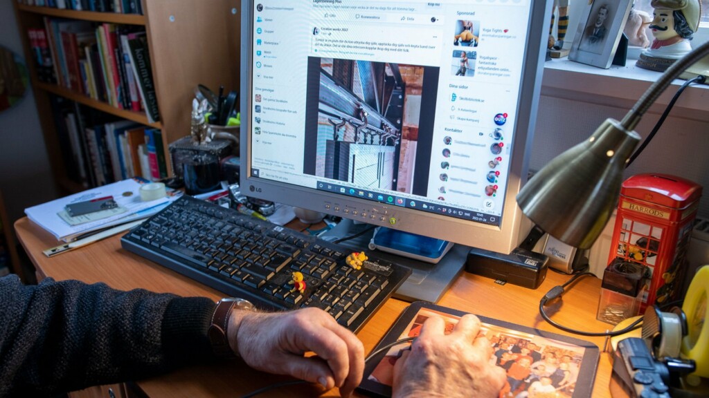 En äldre person sitter vid en dator med sociala medie-konto på skärm framför sig.