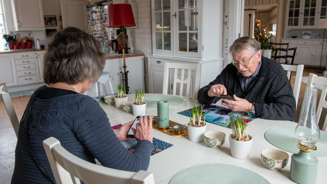 Man och kvinna sitter mitt emot varndra vid ett köksbord, båda har en smartphone i handen