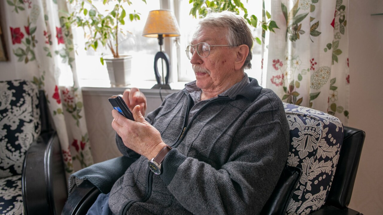 Äldre man sitter i en fåtölj och tittar på sin smartphone