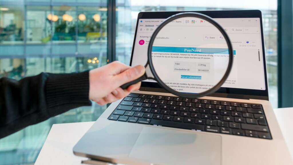 Hand som håller förstoringsglas mot en datorskärm som visar ett bluffmejl