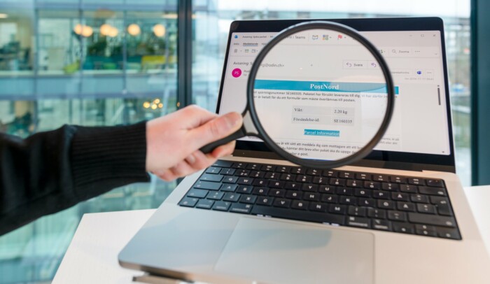 Hand som håller förstoringsglas mot en datorskärm som visar ett bluffmejl