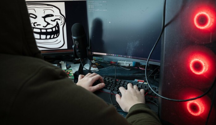 Person sitter vid sin dator, på skärmen syns ett otäckt ansikte