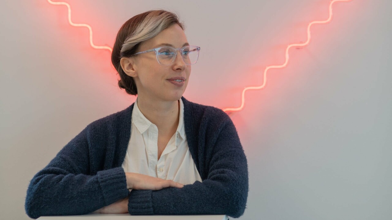 Kvinna står framför en neonskylt i form av ett hjärta och ser ut att fundera.