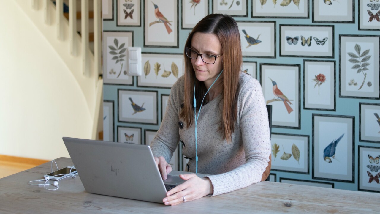 Kvinna sitter hemma vid ett skrivbord och jobbar på laptop.