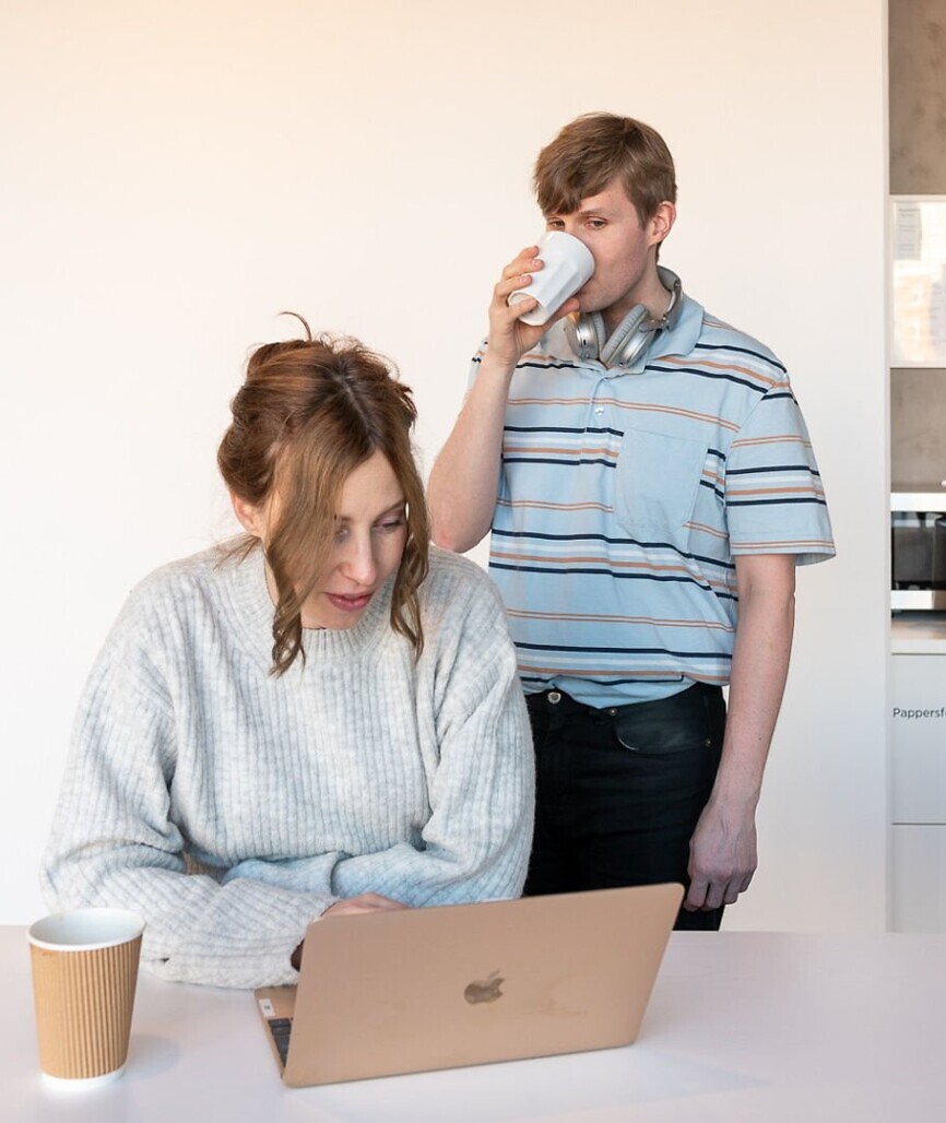 En kvinna sitter vid en laptop, en man står bakom henne och sneglar på skärmen