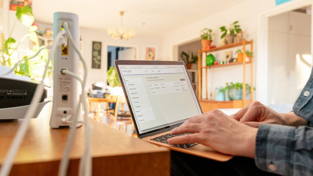 En router och någon som sitter bredvid med en laptop, på skärmen syns routerinställningar.