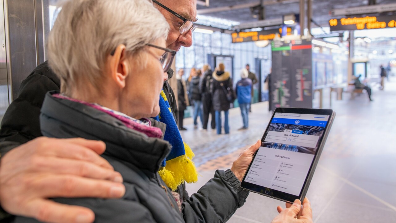 Man och kvinna står vid tunnelbanan och tittar på en surfplatta.