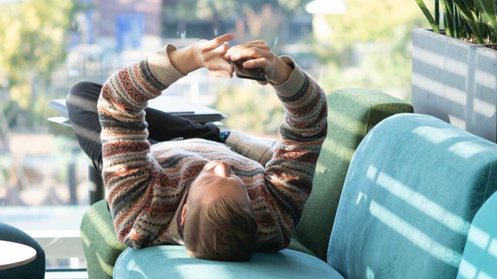 Man ligger i en soffa och tittar på sin mobil