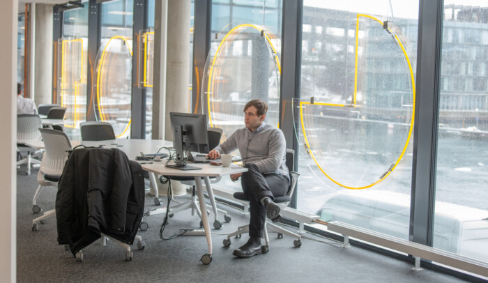 En man sitter vid ett skrivbord, genom fönstret bakom honom syns grått väder.