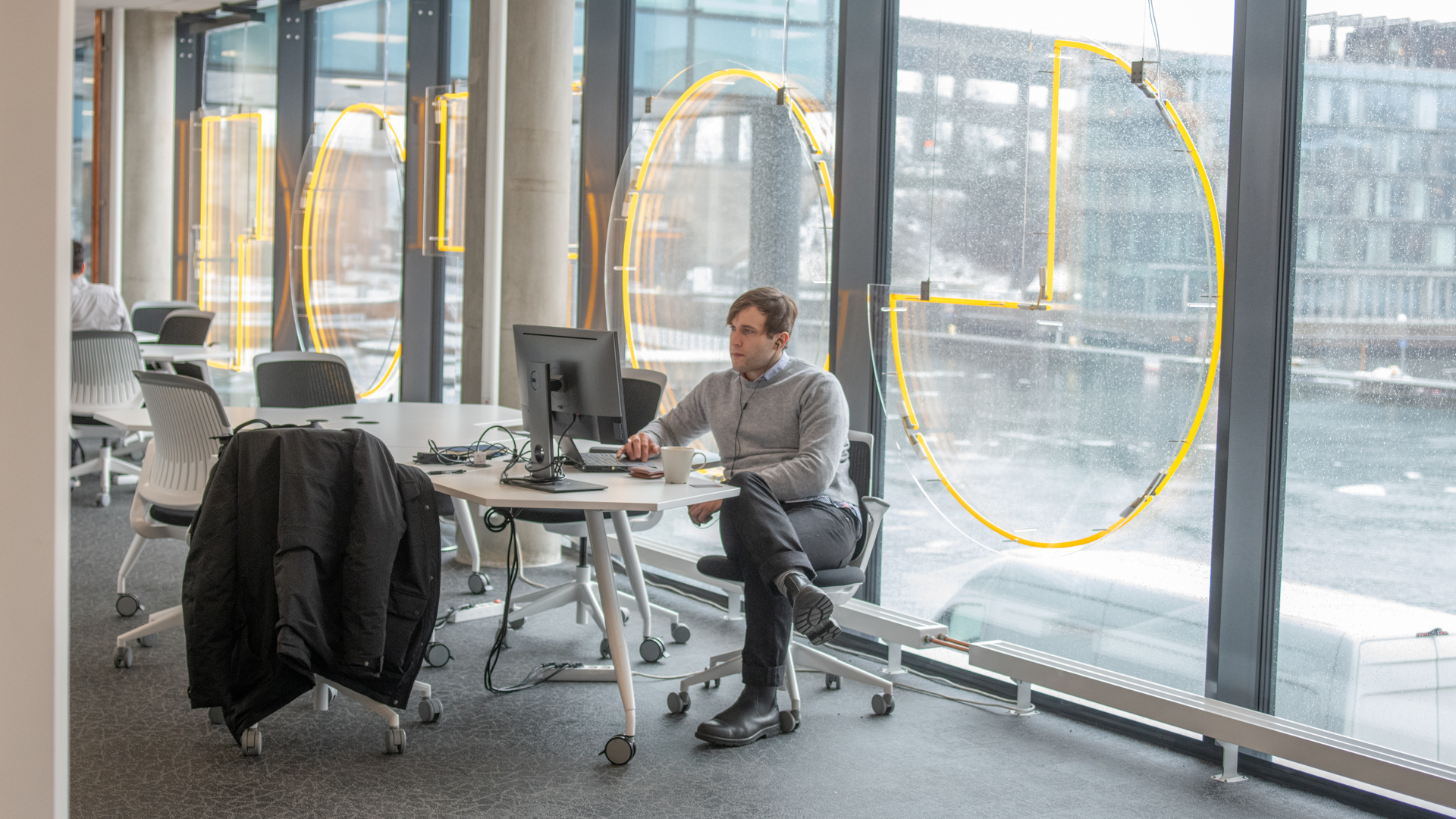 En man sitter vid ett skrivbord, genom fönstret bakom honom syns grått väder.