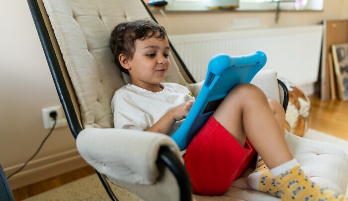 Ett barn sitter i en fåtölj och tittar på sin ipad.