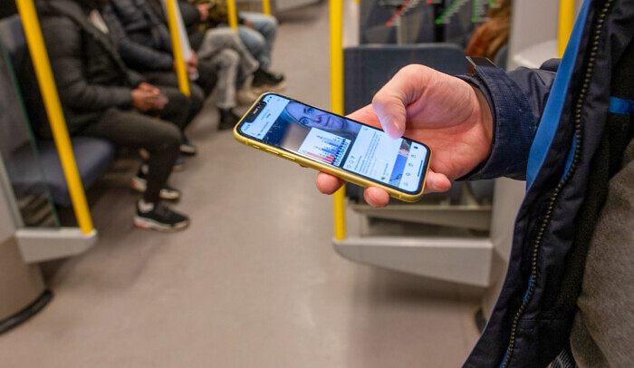 En man scrollar på mobilen på tunnelbanan.