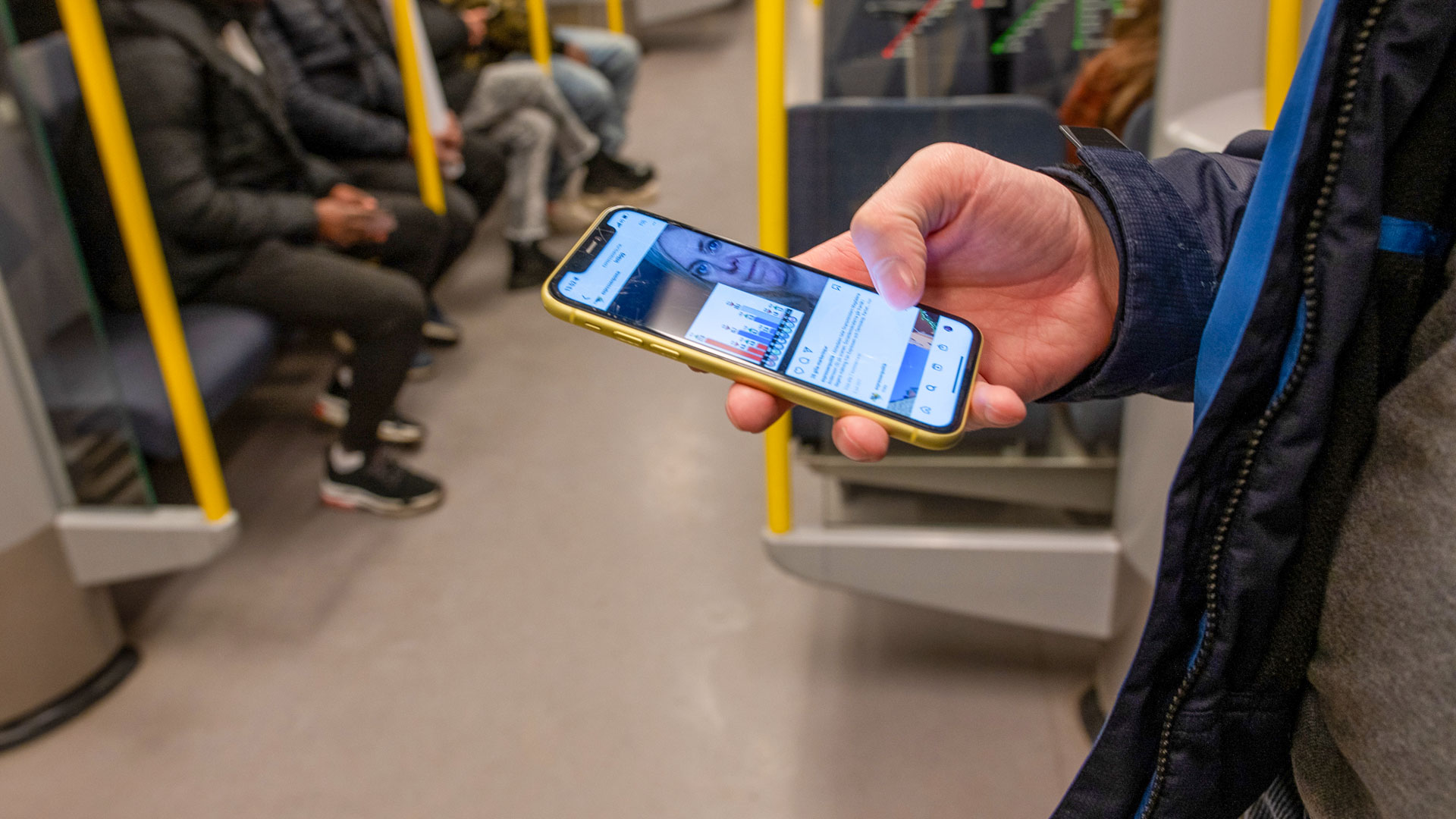 En man scrollar på mobilen på tunnelbanan.