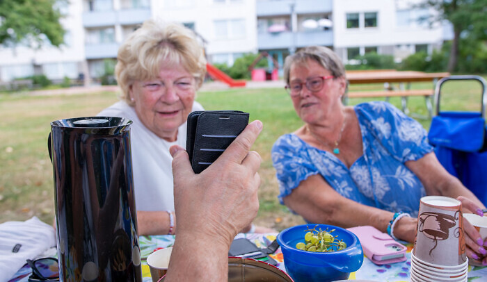 Två äldre kvinnor tittar på en mobilskärm som någon annan håller upp framför dem, de är utomhus.