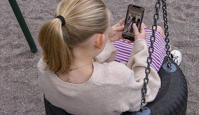 Ung flicka sitter i en gunga och kollar på en mobiltelefon.